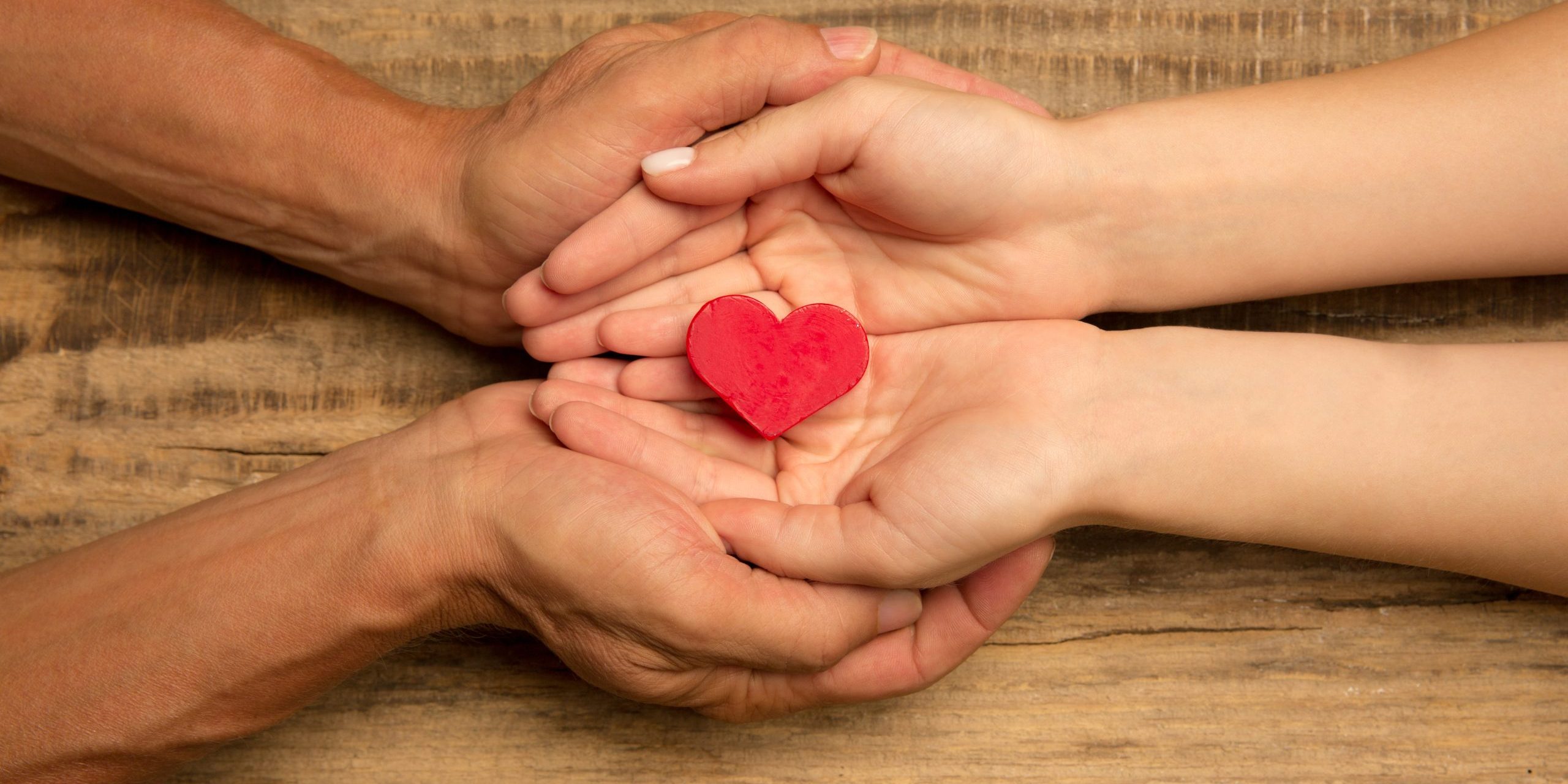 Human hands holding, giving heart isolated on wooden background