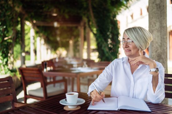 blog june 9 Mature senior woman writing to notebook or diary at a cafe